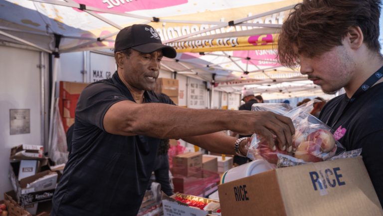 A man in black shirt holding box at outdoor market.